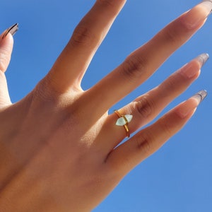 May include: A gold ring with a light blue gemstone in the shape of a rhombus.