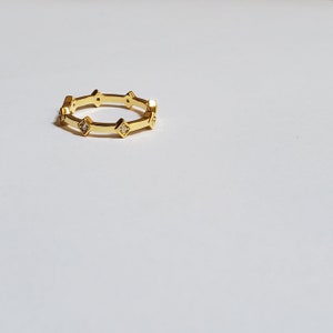 May include: A gold ring with small diamonds set in square shapes around the band.