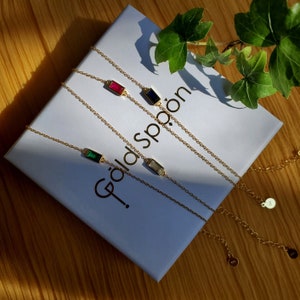 May include: Four gold necklaces with different colored gemstone pendants on a white box with the text "Gold Spoon" printed on it. The gemstones are red, blue, green, and clear.