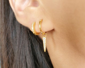 May include: Gold hoop earrings with a dangling spike earring featuring clear cubic zirconia stones.