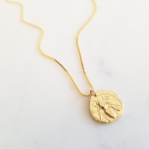 Puede incluir: Un collar de cadena dorada con un colgante de moneda de oro que presenta un diseño de abeja detallado.