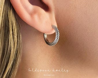 May include: A close-up of a silver hoop earring with a ribbed design. The earring is in a person's ear. The image also includes the text "Goldspoon Jewelry" and "Minimalist".