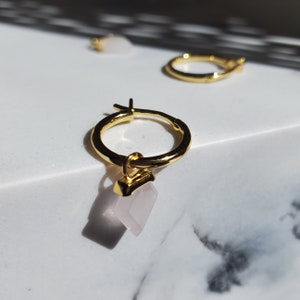 May include: Gold hoop earrings with a dangling pink crystal charm. The earrings are simple and elegant, perfect for everyday wear.
