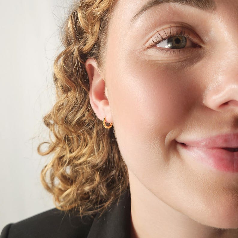 May include: A close-up of a person's face with a small gold hoop earring in their left ear.