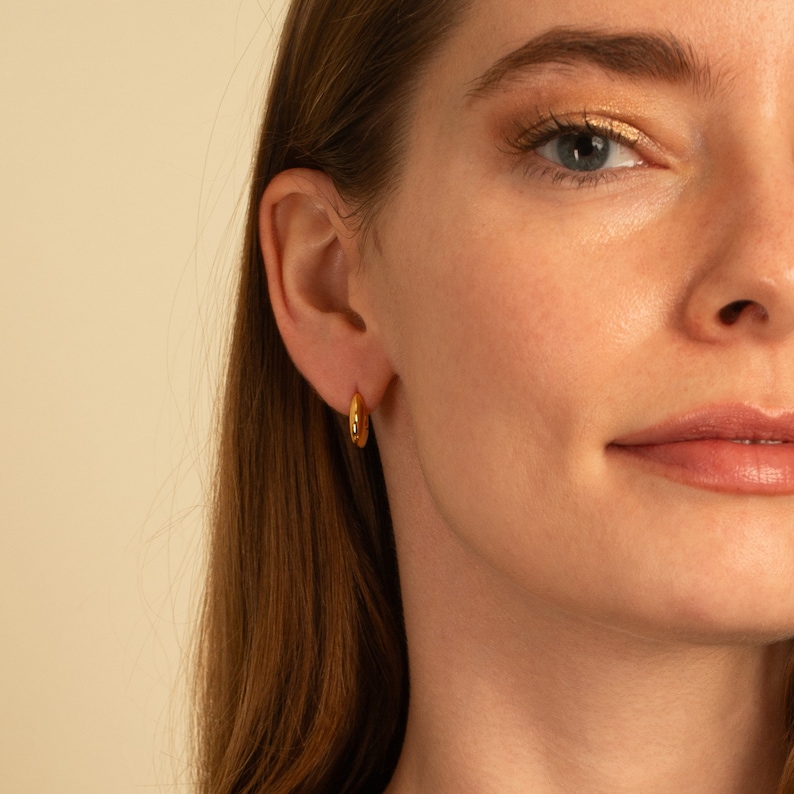 May include: A close-up of a person's ear wearing a gold hoop earring.