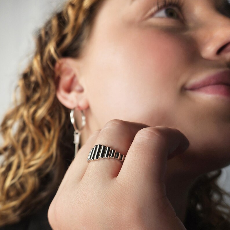 May include: A silver ring with a unique design featuring a series of stacked, vertical, rectangular shapes.