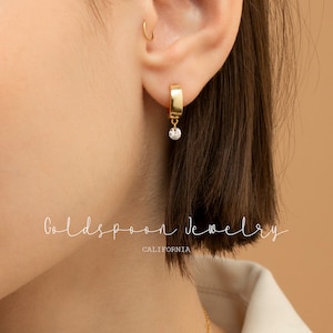 May include: Gold hoop earrings with a dangling diamond-shaped stone. The earrings are made of gold and have a simple, elegant design.  Goldspoon Jewelry CALIFORNIA.