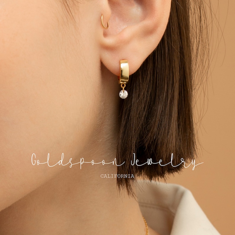 May include: Gold hoop earrings with a dangling diamond-shaped stone. The earrings are made of gold and have a simple, elegant design.  Goldspoon Jewelry CALIFORNIA.