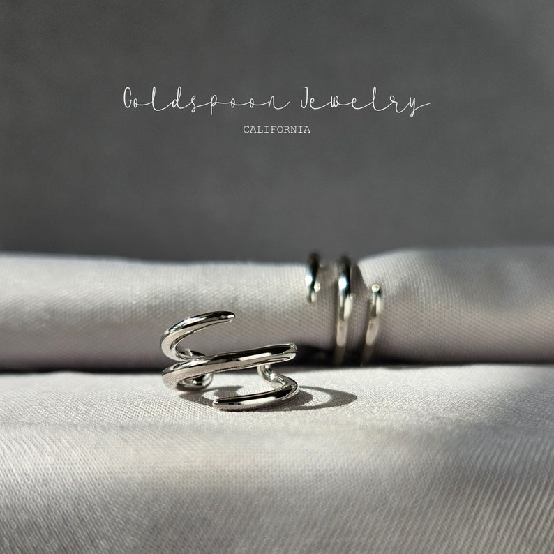 May include: Two silver rings with a twisted design. The rings are on a white fabric background. The text "Goldspoon Jewelry California" is visible at the top of the image.