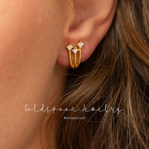 May include: Gold hoop earrings with three small hoops and three tiny cubic zirconia stones. The earrings are minimalist and delicate.