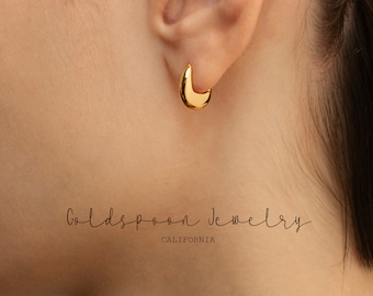May include: Gold hoop earrings in a half-circle shape. The earrings are worn in a person's ear. The text "Goldspoon Jewelry California" is visible below the earrings.