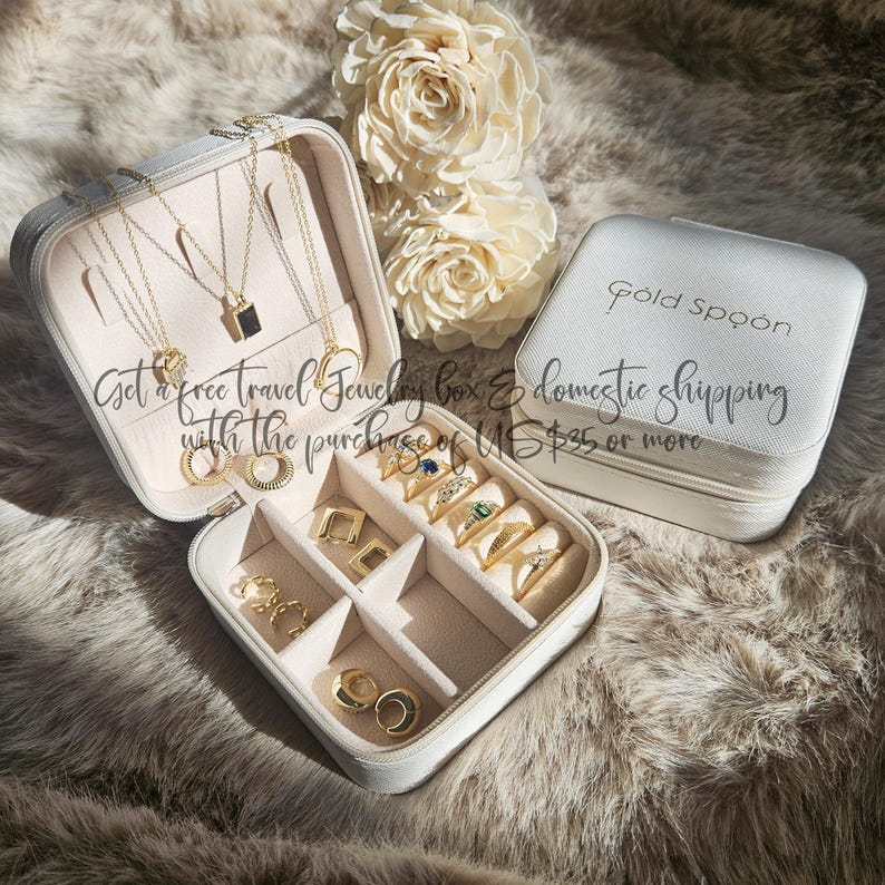 May include: A white travel jewelry box, open to reveal gold necklaces and rings. The box is filled with gold jewellery, including rings and necklaces. The closed box has the text "Gold Spoon". The text "Get a free travel jewelry box" is also visible.