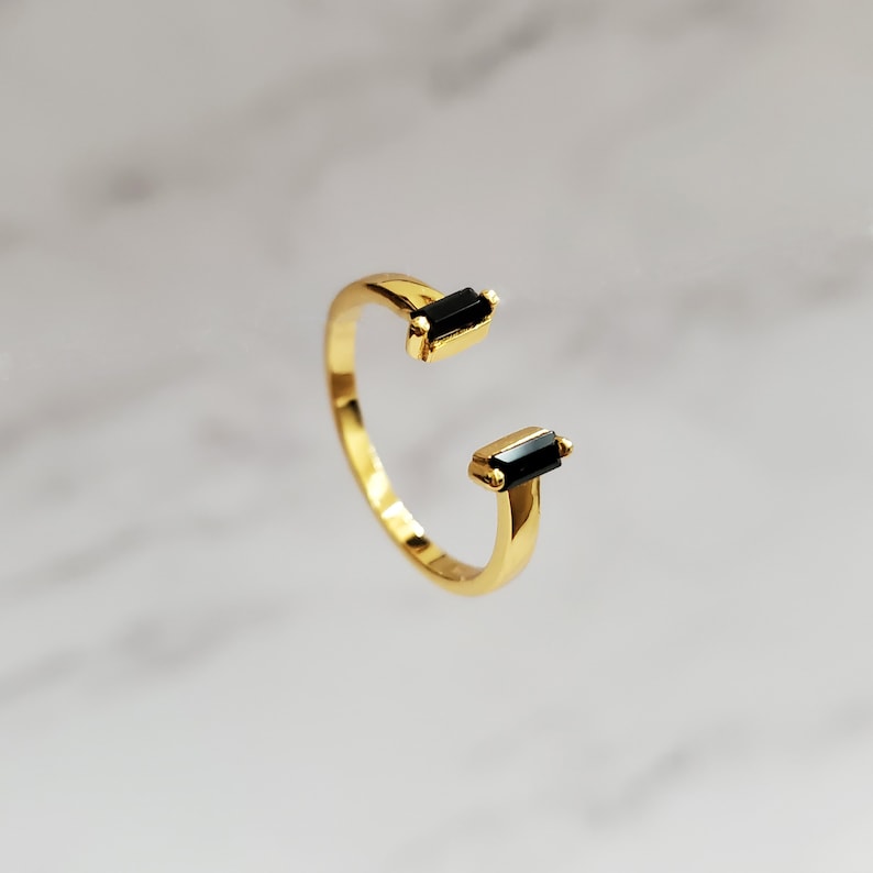 May include: Gold ring with two black rectangular stones. The ring is open on one side.
