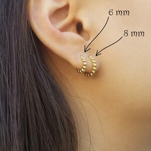 May include: Two gold hoop earrings with a beaded design. The smaller hoop is 6 mm in diameter and the larger hoop is 8 mm in diameter.