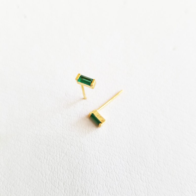 May include: A pair of gold earrings with emerald green rectangular stones.