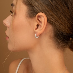 May include: A close-up of a person's ear with a silver hoop earring. The earring is a simple, smooth design.