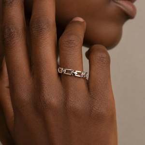 May include: A silver-toned ring featuring a continuous chain-link design. The band is composed of small, rectangular, interlocking metal links that form a uniform, repeating pattern around the entire circumference of the finger.