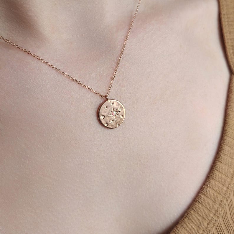 May include: A rose gold necklace with a round pendant featuring a textured design with a star in the center.