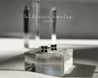 May include: A pair of silver stud earrings with a black square design. Each earring features a small square with four black stones set in a silver frame.