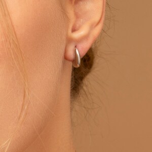 May include: A close-up of a person's ear wearing a small, silver hoop earring.