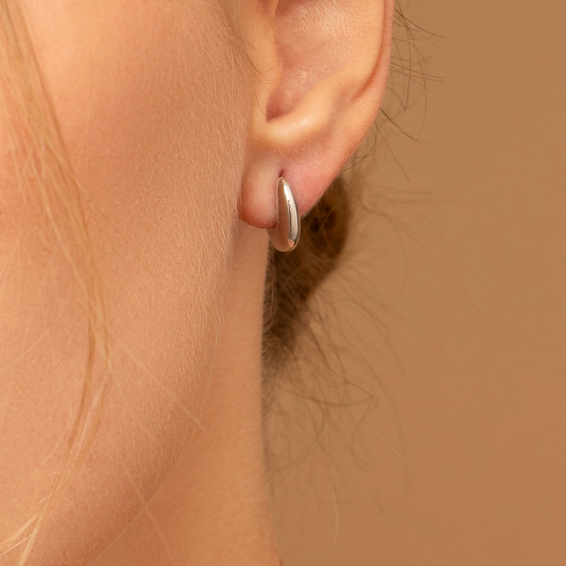 May include: A close-up of a person's ear wearing a small, silver hoop earring.
