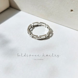 May include: A silver ring featuring a chain link design. The ring is presented on a white surface. The text "Goldspoon Jewelry CALIFORNIA" is below the ring.