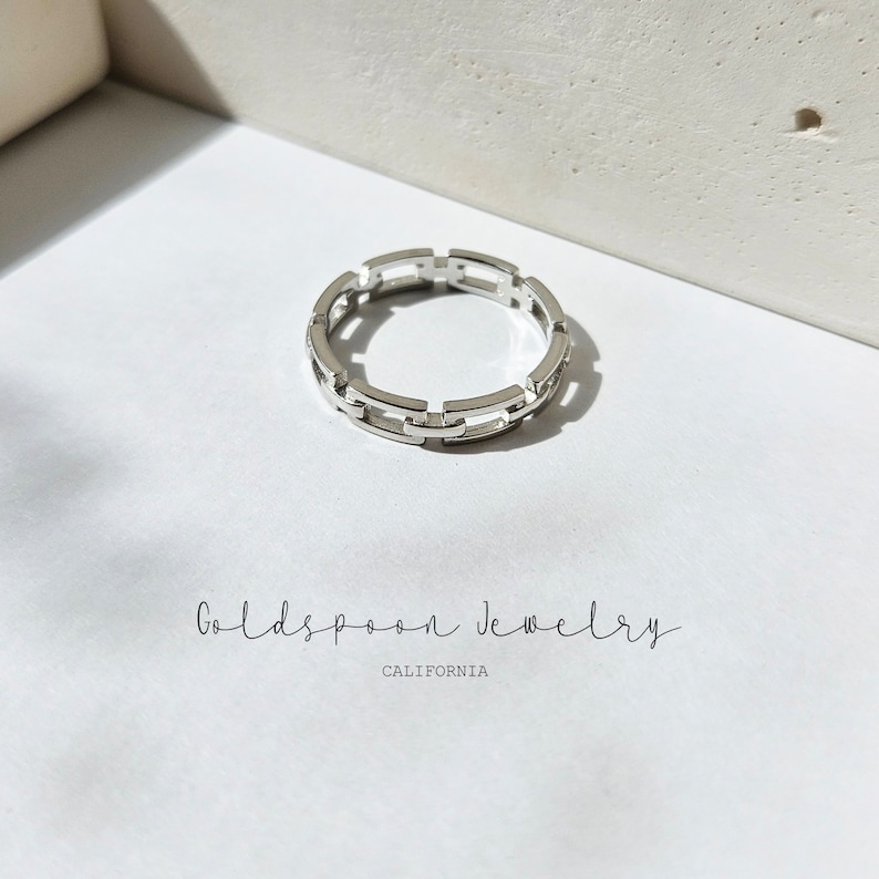 May include: A silver ring featuring a chain link design. The ring is presented on a white surface. The text "Goldspoon Jewelry CALIFORNIA" is below the ring.