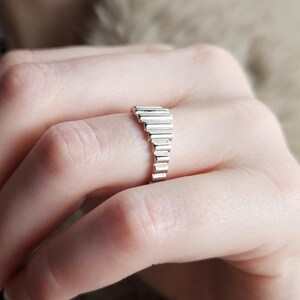 May include: A silver ring with a unique design featuring a series of stacked rectangular shapes.