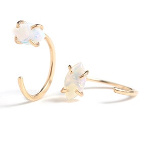 Puede incluir: Dos anillos abiertos de oro, cada uno con una piedra de &oacute;palo iridiscente de corte marquesa sujeta por cuatro garras. Los anillos tienen una banda de oro lisa y pulida que no forma un c&iacute;rculo completo, creando un dise&ntilde;o con abertura.