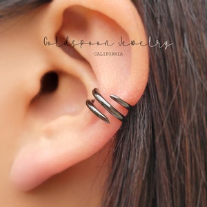 May include: Black ear cuff with three curved, pointed prongs. The cuff is worn on the upper part of the ear.
