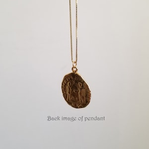 May include: Gold pendant necklace with a round coin-shaped pendant featuring an embossed design of two figures. The pendant is hanging from a delicate gold chain.