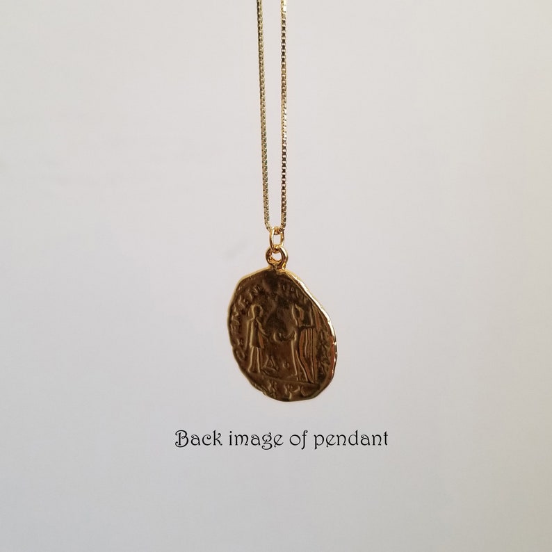 May include: Gold pendant necklace with a round coin-shaped pendant featuring an embossed design of two figures. The pendant is hanging from a delicate gold chain.