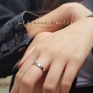 May include: A silver ring with five small black stones set in a row. The ring is on a person's finger. The text "Goldspoon Jewelry California" is visible in the background.