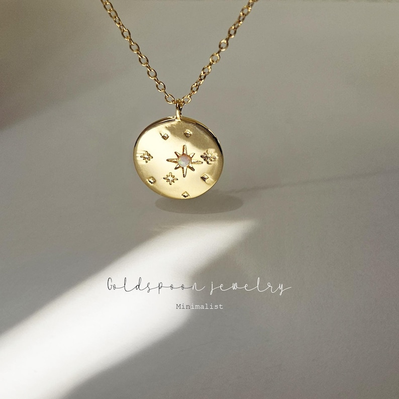 May include: Gold necklace with a round pendant featuring a star with a small opal stone and smaller stars around it. The pendant is on a delicate gold chain.