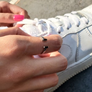 May include: A silver ring with two black rectangular stones. The ring is worn on the index finger of a hand.