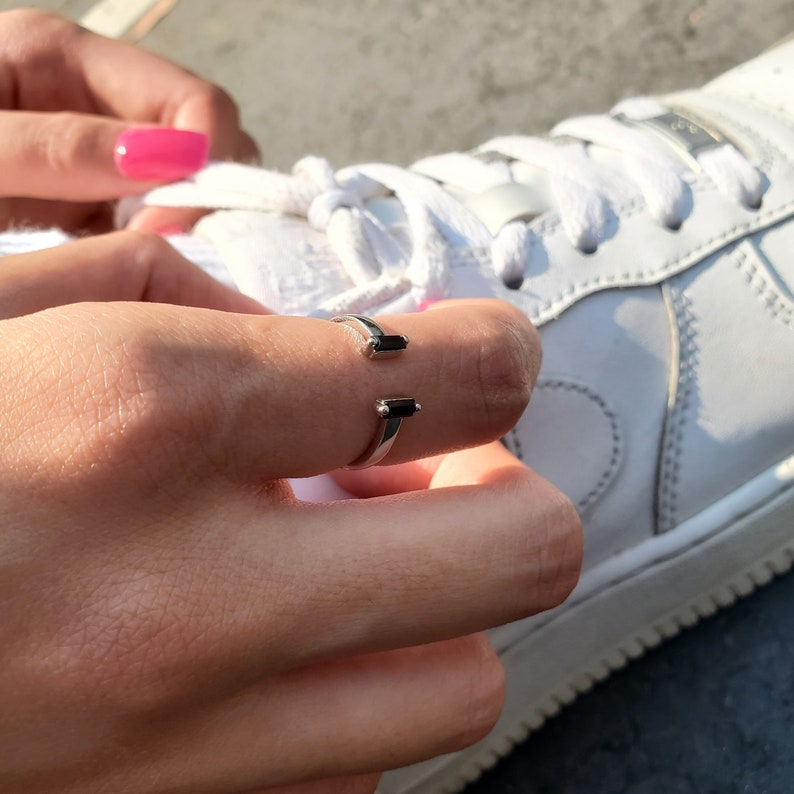 May include: A silver ring with two black rectangular stones. The ring is worn on the index finger of a hand.