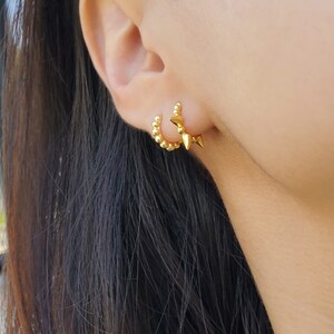 May include: A pair of gold hoop earrings. One hoop is studded with small gold balls, the other has three gold spikes.
