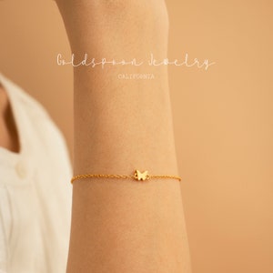 May include: A delicate gold chain bracelet with a small butterfly charm. The bracelet is on a person's wrist.