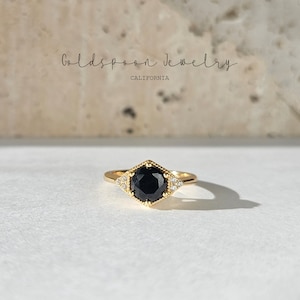 May include: A gold ring with a black gemstone surrounded by smaller white gemstones. The ring is set in a geometric design.