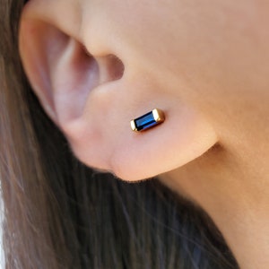 May include: Gold stud earrings with a blue rectangular gemstone.