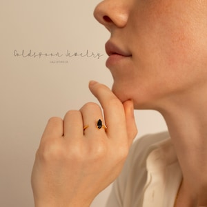 May include: A gold ring with a black marquise-shaped gemstone. The ring is open and wraps around the finger.