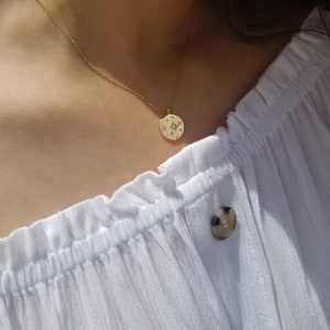 May include: A gold necklace with a round pendant featuring a compass design with a star in the center and small diamonds around the edge.