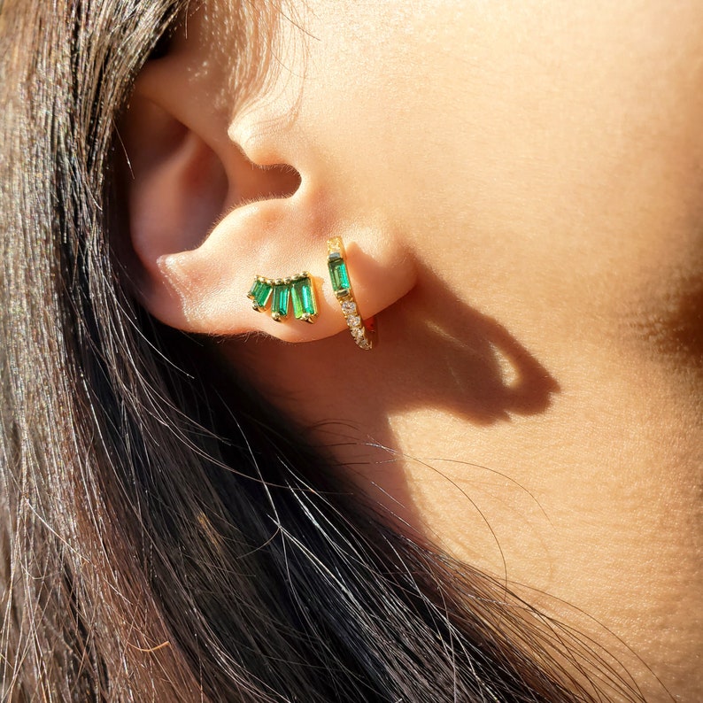 May include: A pair of gold earrings with green emerald stones. One earring is a hoop with a row of small diamonds, the other is a cluster of emerald stones.