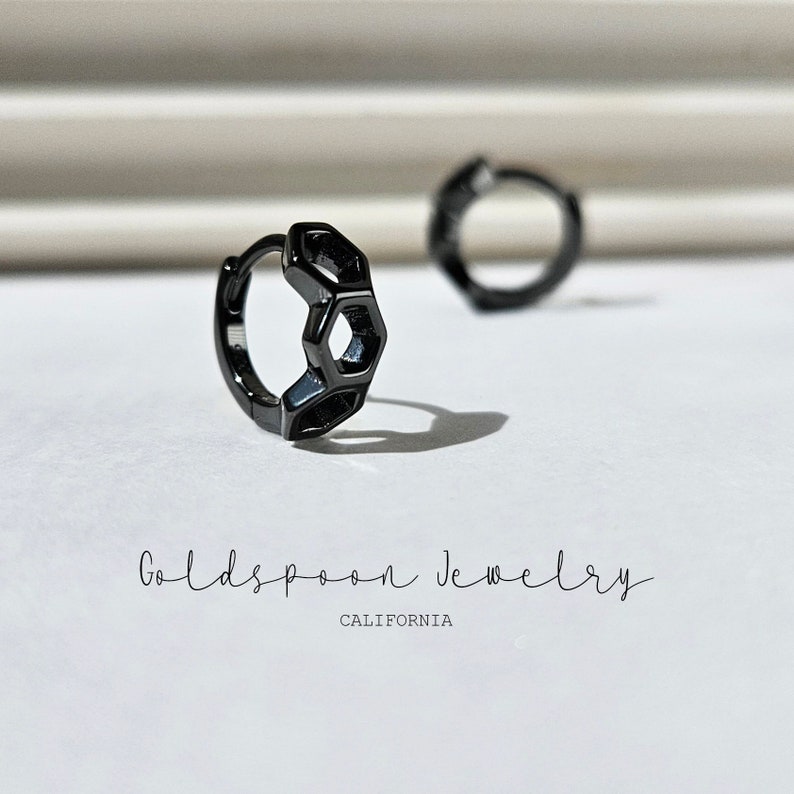May include: A pair of black hoop earrings with a geometric hexagonal design. The earrings are made of metal and have a polished finish.