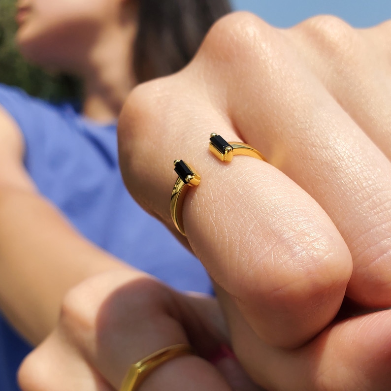May include: A gold ring with two black rectangular stones. The ring is open and adjustable.