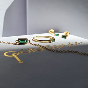 May include: A set of emerald green gemstone jewelry on a white box with the text "Goldspoon". The set includes a necklace, a ring, and a pair of earrings.