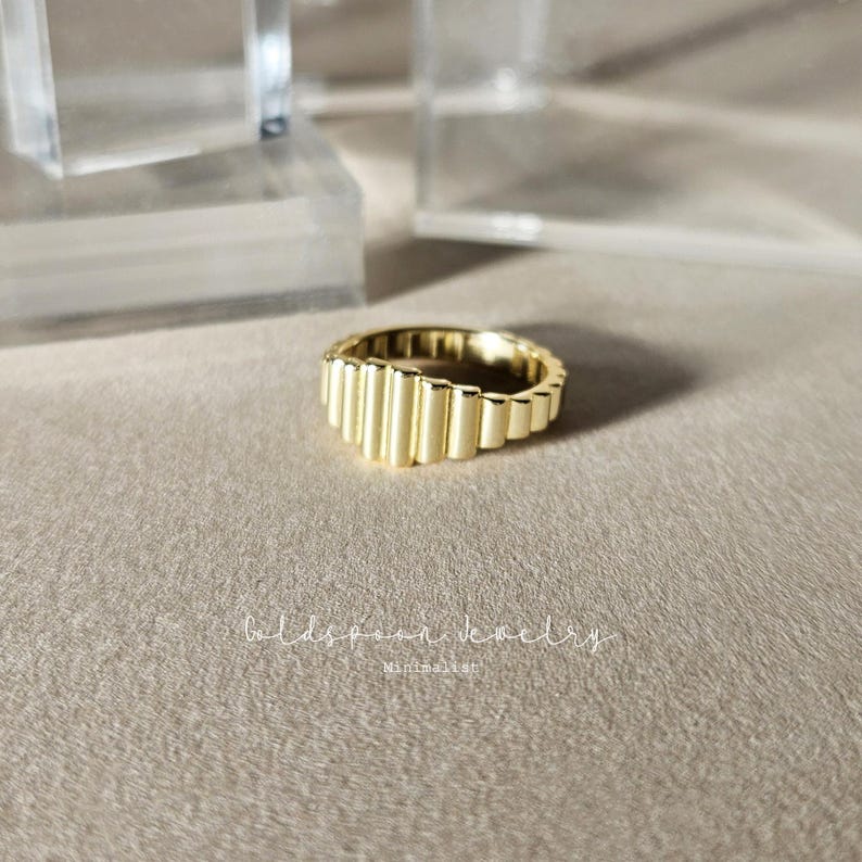 May include: Gold ring with a unique, geometric design. The ring is made of a series of stacked, rounded, vertical bars that create a textured, modern look.