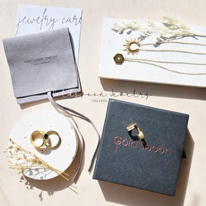 May include: A set of gold jewelry in a black box with the words "Gold Spoon" printed on the top. The jewelry includes a pair of hoop earrings, a ring with a black stone, and a necklace with a sun and a hexagon pendant.