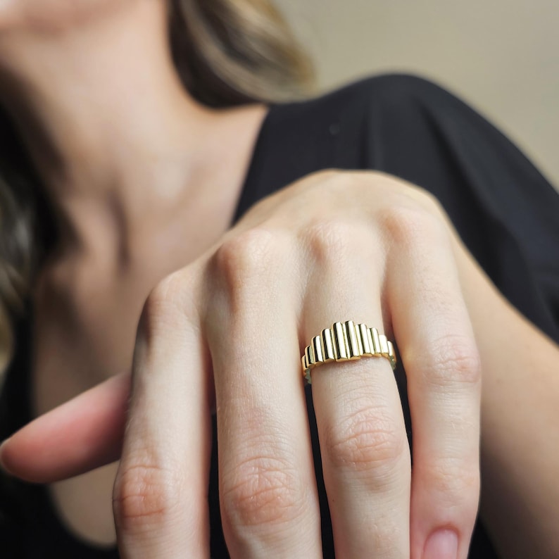 May include: A gold ring with a textured, ridged design. The ring is worn on a finger.