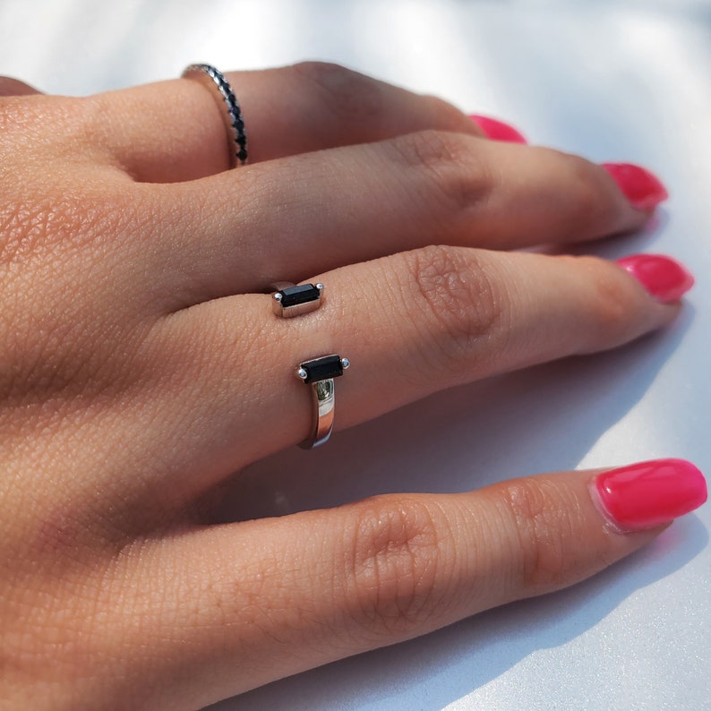 May include: A silver ring with two black rectangular stones. The ring is on a person's finger.